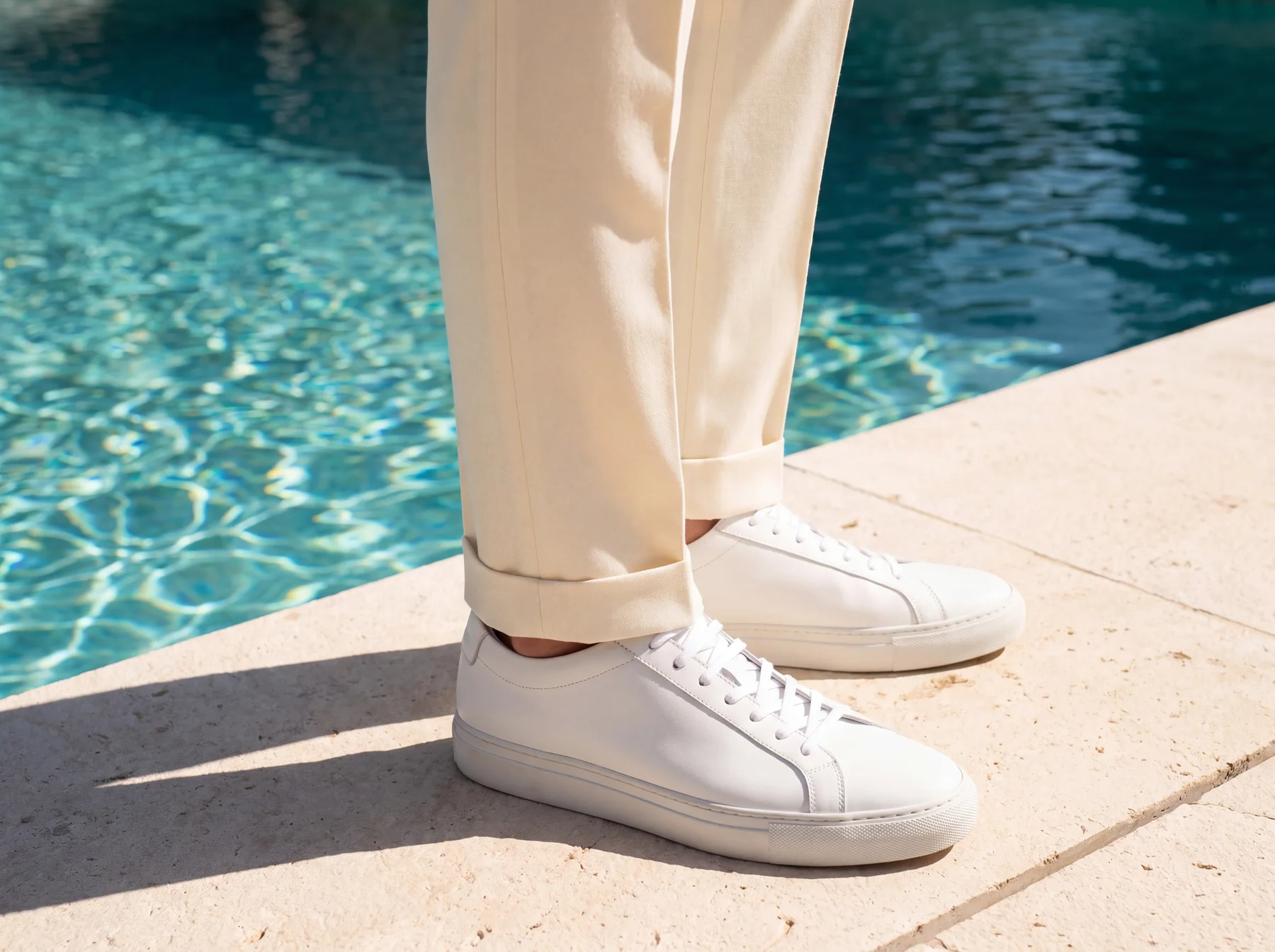 The deep turn-up of the ivory Palazzo trouser breaking over white leather sneakers beside a pool.