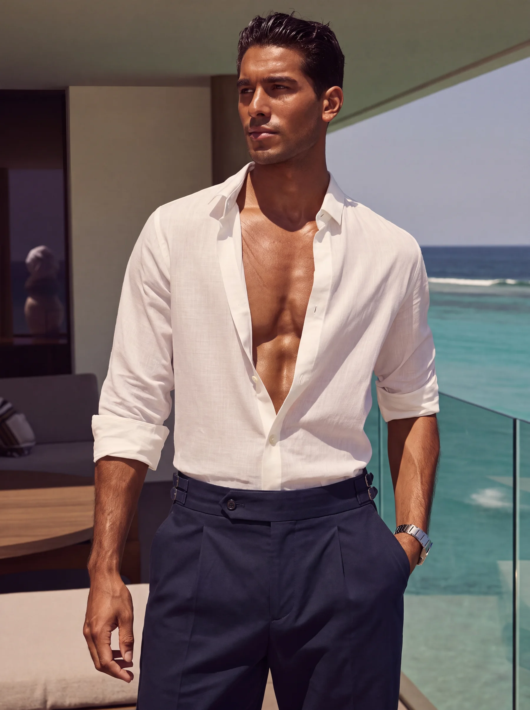 A young Sri Lankan man at a beach club in a white linen long-sleeve shirt tucked into navy Valdoro trousers.